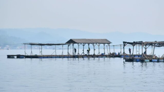 People fishing on floating cages on a calm sea in Lampung with fishing villages in the distance