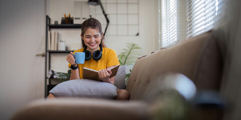 Happy young woman read book on sofa at home. Lifestyle freelance relax in living room. lifestyle relaxation concept - obrazy, fototapety, plakaty