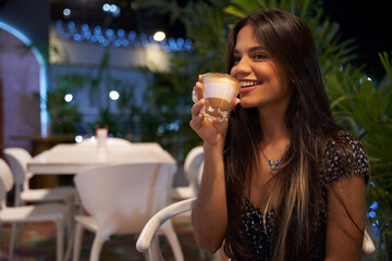 Mujer Joven latina  de cabello castaño largo tomando cafe sentada 