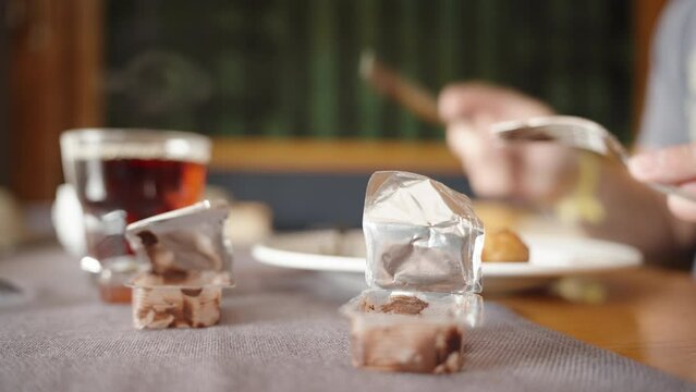 Breakfast in a restaurant, steam rises from hot tea, opened jars of portioned chocolate, men's hands with a fork and spoon. Close-up.