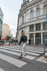 Beautiful young fashion model girl in fashion urban clothes walks in the city at a pedestrian crossing