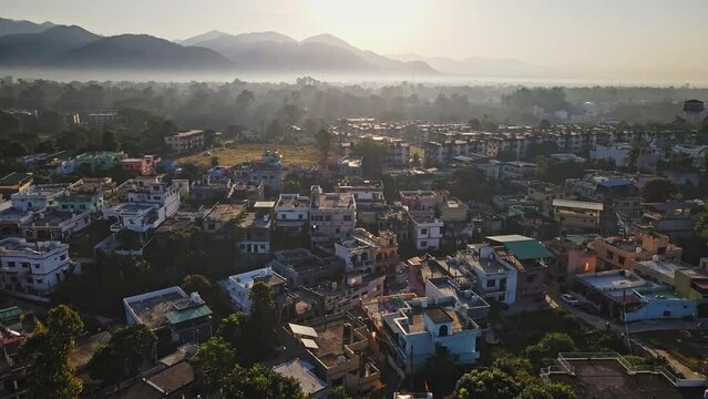 An aerial view of Dehradun, an Indian city during sunrise or sunset, with cloudy weather and rows of residential houses surrounded with greenery. The Himalayan city is surrounded by rainforest.