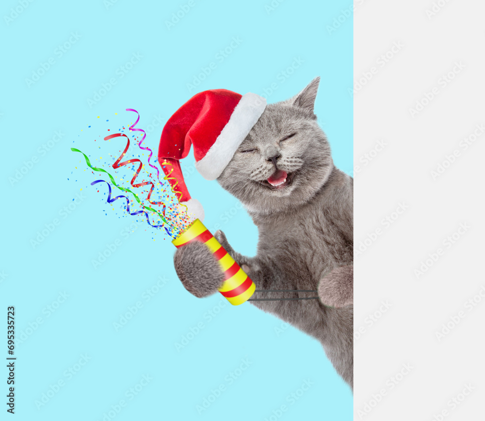 Aufkleber Happy cat wearing red santa hat holds exploding firecracker and looks from behind empty white banner. Isolated on blue background