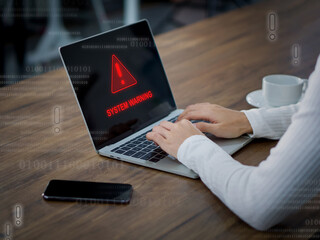 A woman looks worried while using her laptop which displays a red warning sign on the screen.