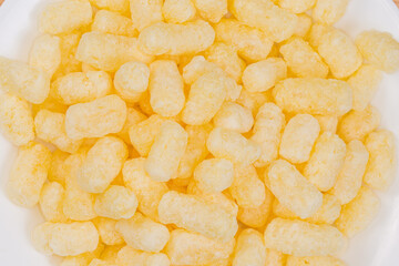 Heap of sweet corn puffs on white plate, top view