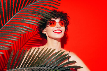 Fashion beauty portrait of young smiling brunette woman with evening stylish  makeup and perfect clean skin. Sexy model with curly short hair posing in studio. With red bright lips. Tropical palm leaf