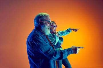 Excited and emotional senior man, and little girl watching movie in 3D glasses over gradient orange...