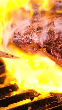 Grilled meat steak on stainless grill depot with flames on dark background. Food and cuisine concept.