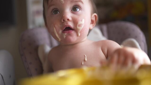 baby eats dirty. happy family lifestyle a kid toddler concept. baby girl dirty sitting messing with food at the table for feeding in the kitchen. grimy toddler in the kitchen