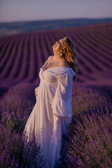 woman poses in lavender field at sunset. Happy woman in white dress holds lavender bouquet. Aromatherapy concept, lavender oil, photo session in lavender