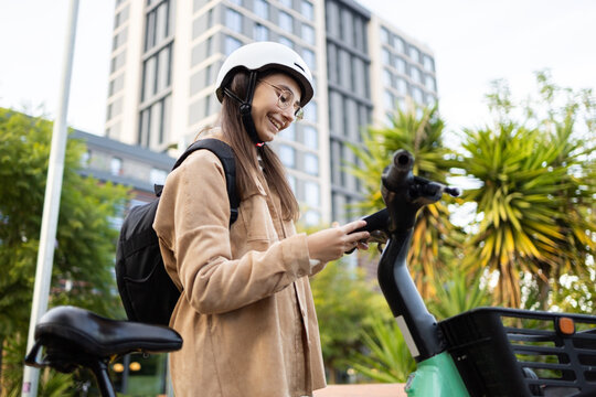 Young woman with helmet using smartphone on city e-scooter