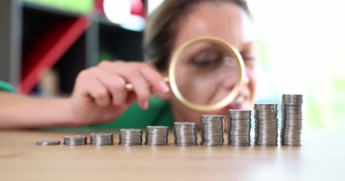 Emotions of excited greedy business woman looking at growing stack of coins through magnifying glass. Growth in financial cash income
