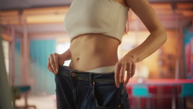 Close Up Slow Motion on the Waste of Beautiful Fit Woman Trying on her Old Jeans Before Diet. Female Noticing Difference Made by a Healthy Lifestyle. Results of Healthy Eating and Working Out