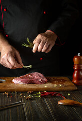 Adding rosemary to meat by the hand of the cook for aroma and taste. The process of cooking beef steak on the kitchen table with spices and pepper