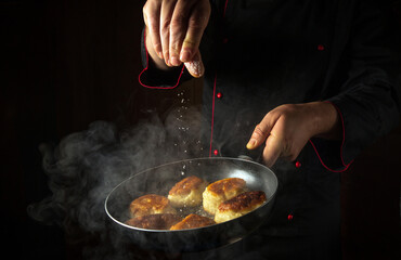 Frying delicious oladyi for breakfast. The cook salts the pancakes in a frying pan. Black space for menu or recipe