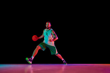 Dynamic shot capturing skilled basketball player in action, focused and determined during intense training session against black background in neon light.