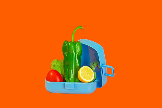 Colorful lunchbox with fresh vegetables on orange background