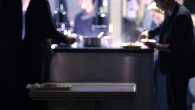 Defocused view of chefs preparing food for a large reunion while waiters swiftly arrive to collect the dishes, capturing kitchen bustle