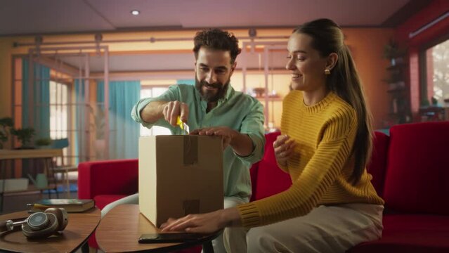 Portrait of a Man Bringing a Long-awaited Parcel to his Beautiful Young Wife at Home. Excited Couple Open Cardboard Box while Sitting on a Couch in their Bright Stylish Living Room