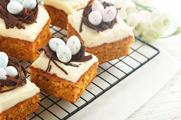Easter carrot cake bars decorated with chocolate nest and chocolate candy eggs blossoming cherry or apple flowers on rustic light wooden backgrounds. Easter holiday meal. Traditional Easter food.