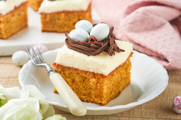 Easter carrot cake bars decorated with chocolate nest and chocolate candy eggs blossoming cherry or apple flowers on rustic light wooden backgrounds. Easter holiday meal. Traditional Easter food.