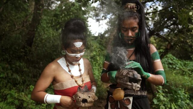 Confident young female Mayan warriors in traditional dress and body painting performing a traditional smoking ritual with incense copal burners in Mexico