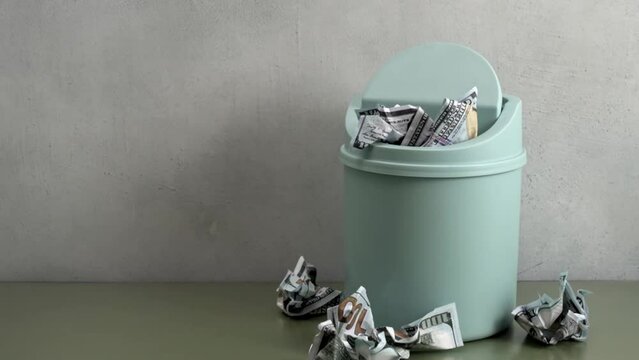 Crumpled dollar bills fall into the trash bin. Lean spending concept