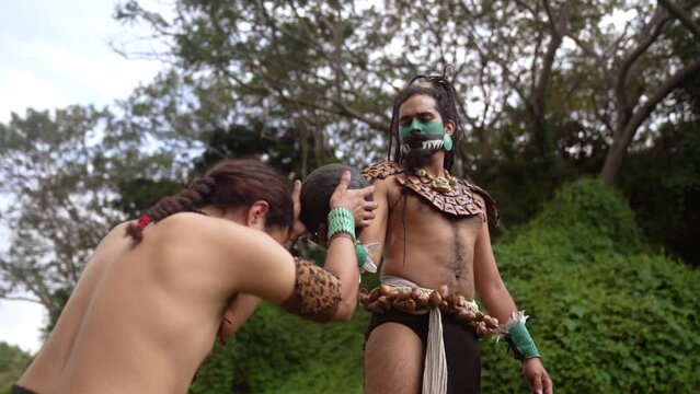 From below Mayan male warriors in traditional body costumes and face paint engaging in the ancient Mesoamerican ballgame with a dark ball in a grass near ancient ruins in Mexico