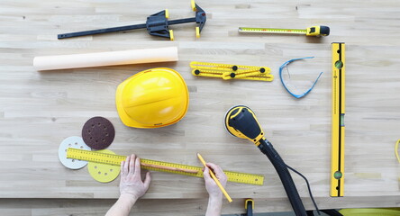 Top view of engineer markup for construction site. Working equipment on table. Foreman hands holding ruler and pencil. Yellow helmet of desk. Renovation concept