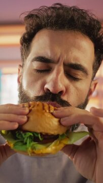 Vertical Screen: Tracking Slow Motion Portrait of a Man Who is Enjoying a Delicious Hamburger at Home. Colorful Setting For a Happy Male Who Ordered Fast Food Delivery, Approving of the High Quality