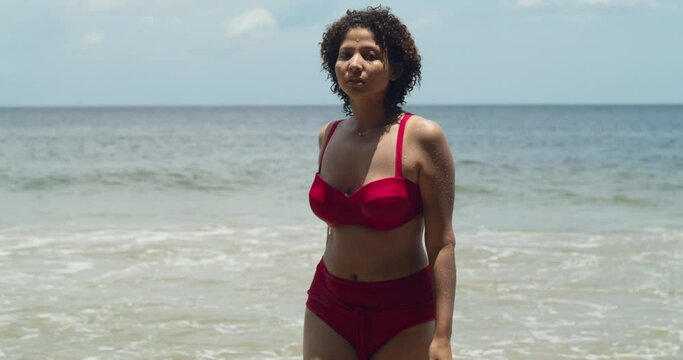 The beauty of a sunny day on a tropical island beach is captured by a young girl with curly hair in a striking red bikini walking on the beach