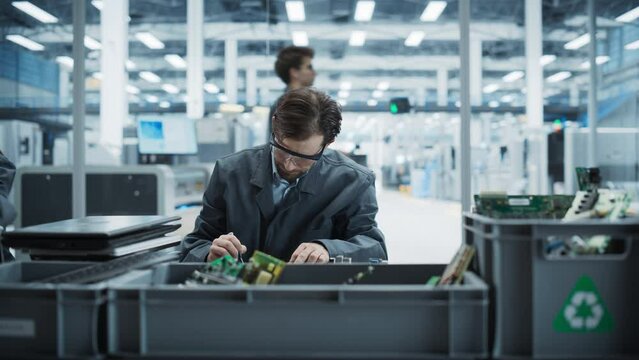 Caucasian Male Worker Disassembling Old Laptops To Recycle Electronic Components For Sustainable Microchip Production At Electronics Factory. Man Unscrewing Motherboards And Sorting Parts In Boxes.
