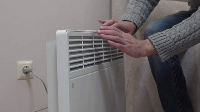 a man warms his hands near an electric heater, a man warms his frozen hands at home on an electric convector