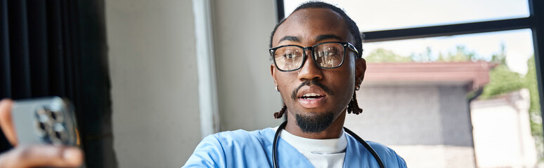 young african american doctor with glasses consulting someone by mobile phone, telemedicine, banner