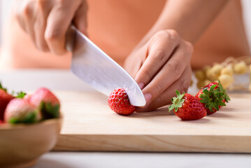 Hand holding kitchen knife and cutting strawberry on wooden board