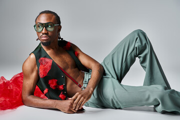 appealing african american man in vibrant attire with red tulle fabric reclining on floor, fashion