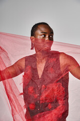 good looking young african american male model posing with vibrant red tulle fabric on gray backdrop