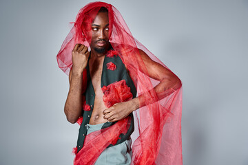 good looking young african american man posing in motion with red tulle fabric and looking away