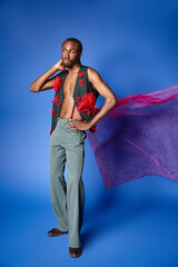 attractive african american man in stylish attire on blue backdrop looking away, fashion concept