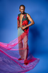 appealing african american man in stylish attire on blue backdrop looking away, fashion concept