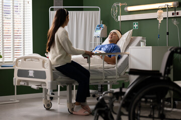 Fototapeta premium The man, post-operation, rests in the hospital bed, surrounded by the care and tenderness of his wife. Her presence is an invaluable support, sustaining hope for a complete recovery