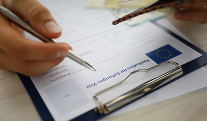 Close-up of male person filling application form for schengen visa holding silver pen. Writing...