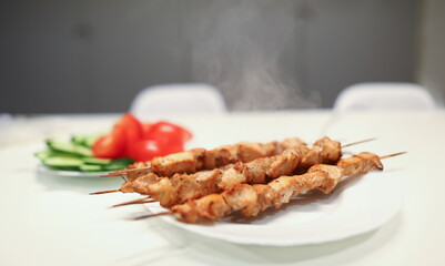 Close-up of delicious grilled chicken pieces on bamboo skewers on plate. Aromatic meat for lunch or dinner. Fresh cucumber and tomato. Home barbeque. Tasty meal and healthy food concept