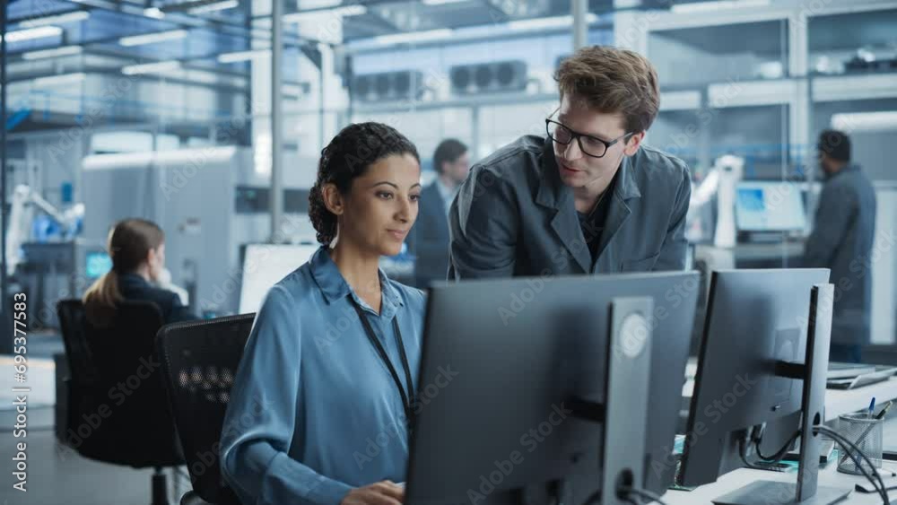 Poster Portrait of a Young Male Assembly Line Worker and Hispanic Female Engineer Collaborating on a Project, Using Computer and Talking in a Factory with Robotic Arms Producing Devices for Tech Industries.
