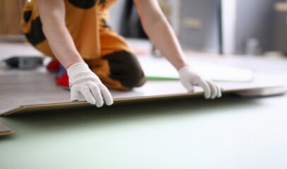 Close-up of adult man installing new laminated wooden floor in room. Professional worker in protective white gloves. Qualified foreman. Construction site concept