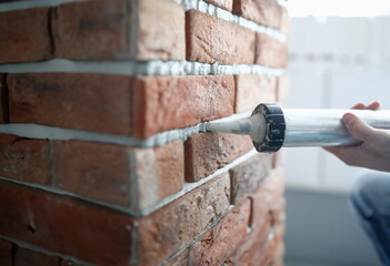 Close-up of professional worker holding fixing foam on construction site. Red brick wall in...