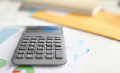 Close-up of black calculator laying on business papers. Equipment to calculate numbers. Tool with buttons on working desktop. Financial report and statistics concept