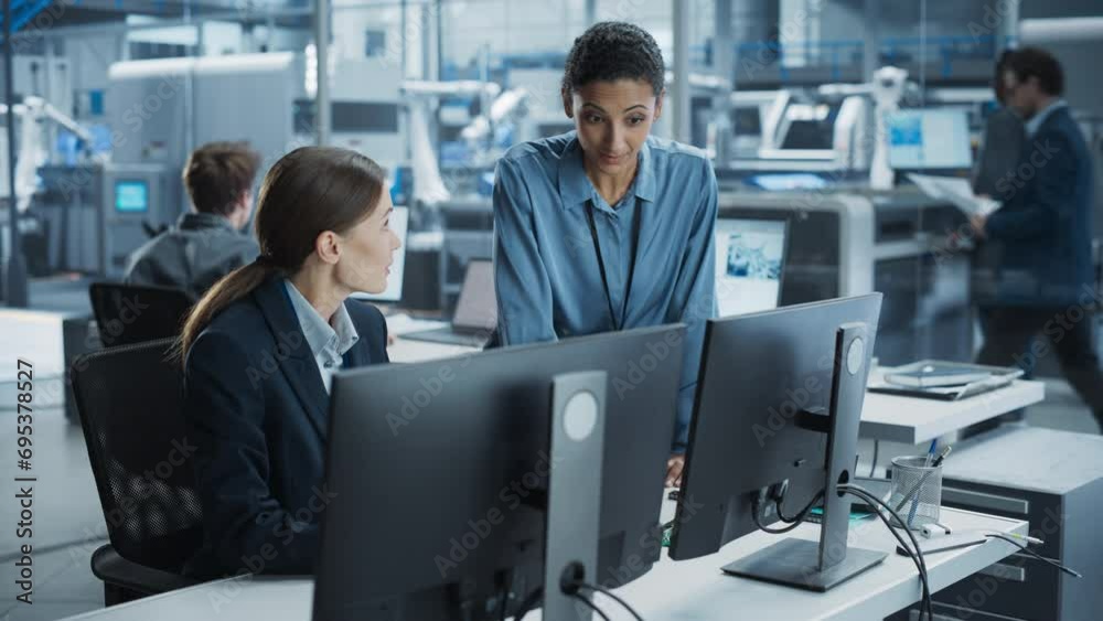 Aufkleber Caucasian Female Engineer And Hispanic Product Manager Using Desktop Computer And Talking At Automated Factory With Robotic Hands. Diverse Colleagues Discussing New High-Tech Devices Production.