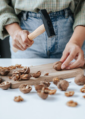 female hands break walnuts with a hammer on a wooden board in a bright kitchen. rows and lots of peeled nuts and shells