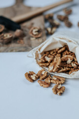 There is a wooden cutting board on a light background with a hammer and walnuts on it. next to it is a white fabric bag with shelled walnuts